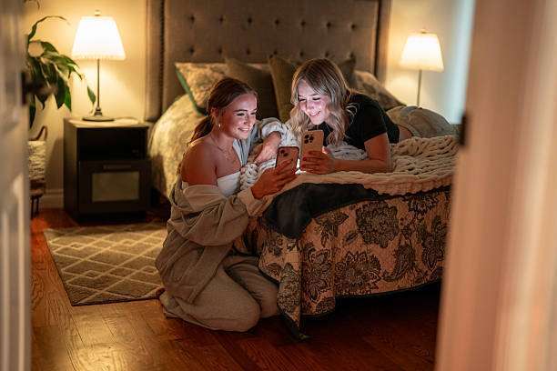 Two young women sit comfortably in a cozy bedroom. Lamp shades