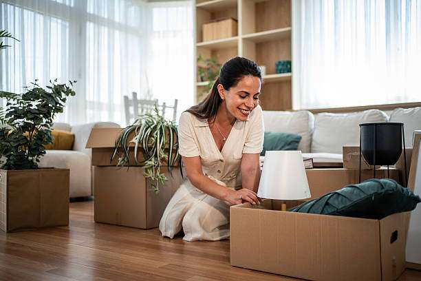 Woman unpacking, holding a white lamp with a modern lamp shade in her new living room.