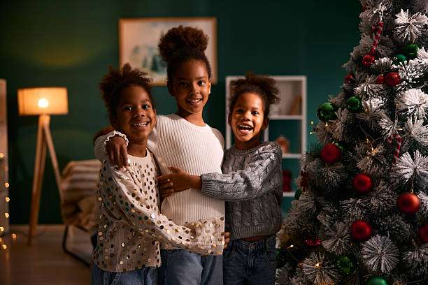 Three smiling children near a Christmas tree with decorative lamp shades.