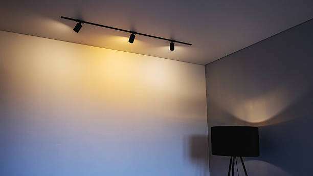 Modern track lighting illuminating wall, with lamp shades visible.