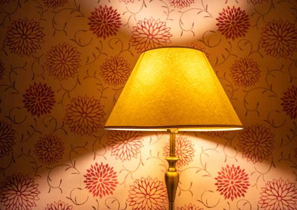 Yellow lamp shade casting warm light on floral wallpaper, creating a cozy ambiance.